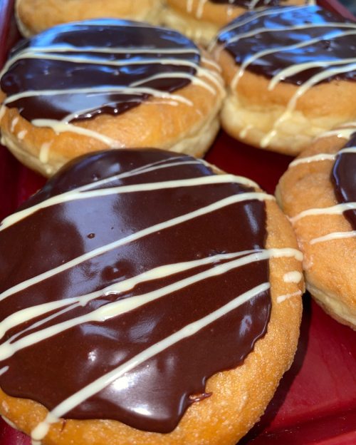 A close-up of glazed donuts topped with chocolate icing and white drizzle, arranged on a red tray.