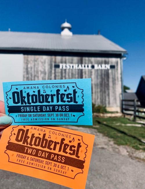 Two colorful Oktoberfest passes held in hand: a blue single day pass and an orange two day pass against a barn backdrop.