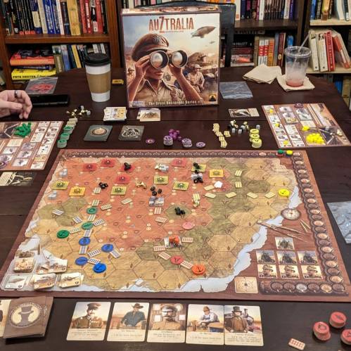 A tabletop game of Australia with a detailed map, tokens, cards, and a game box in a cozy setting.
