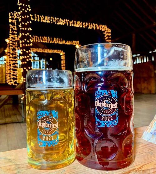 Two beer mugs, one filled with light beer and the other with dark beer, set against a backdrop of twinkling lights.
