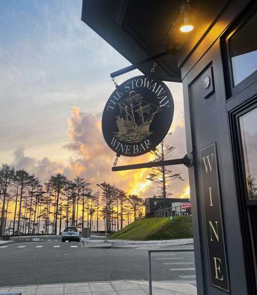 Sign for "The Stowaway Wine Bar" with a ship design, set against a sunset and trees in the background.