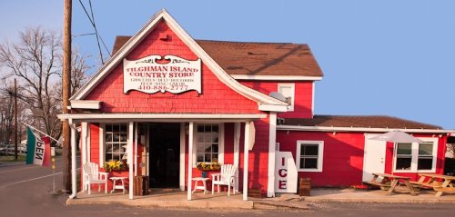 A red country store with a sign reading "Tilghman Island Country Store," featuring white chairs and an "ICE" sign outside.