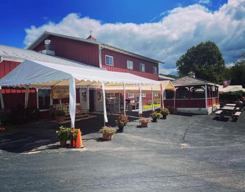 A red barn-style building with a white tent and gazebo, surrounded by flower pots and a paved area.