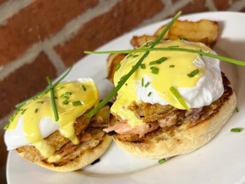 Two poached eggs on toasted English muffins with hollandaise sauce, topped with chives, served with potato wedges.