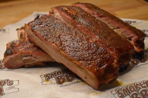 Three succulent, smoked BBQ ribs with a crispy exterior, resting on branded parchment paper.