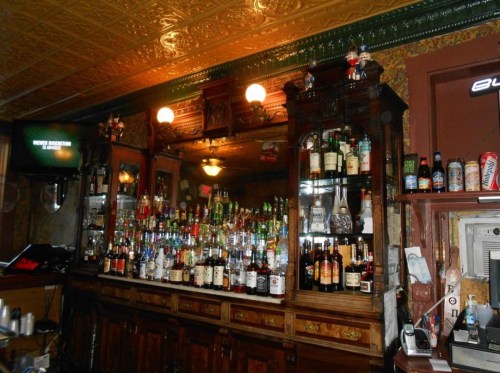 A vintage bar with a mirrored back, showcasing a variety of liquor bottles and ornate wooden cabinetry.