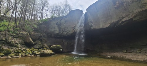 A serene waterfall cascades into a rocky pool, surrounded by lush greenery and towering cliffs.