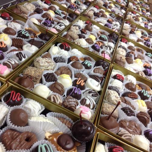 A variety of assorted chocolates arranged in gold boxes, featuring different shapes and colorful decorations.