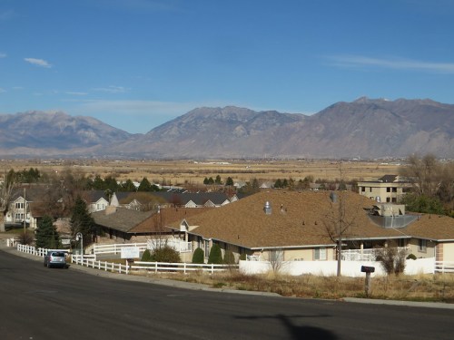 A scenic view of a valley with mountains in the background, featuring houses and a clear blue sky.