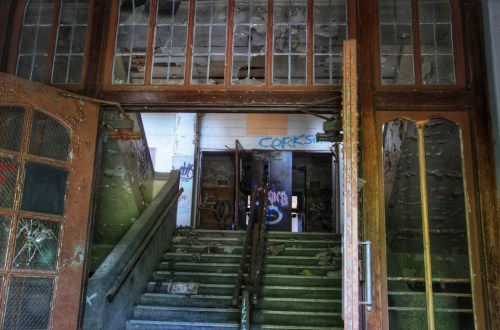 Abandoned building entrance with worn stairs, broken windows, and graffiti on the walls.
