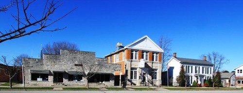 A clear blue sky above three distinct buildings: a stone structure, a brick building, and a white house.