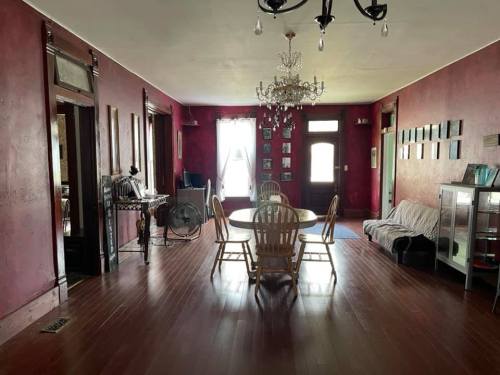 A spacious room with red walls, a chandelier, a round dining table, wooden chairs, and a cozy seating area.
