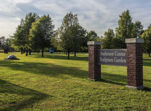 Sign for Anderson Center Sculpture Garden, surrounded by trees and a grassy area under a clear sky.