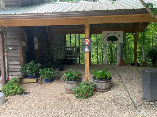 A rustic winery entrance with potted plants, a sign, and a wooden structure surrounded by trees.