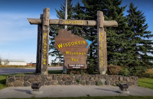 Welcome sign for Wisconsin featuring wooden beams and stone base, highlighting industry, recreation, and agriculture.