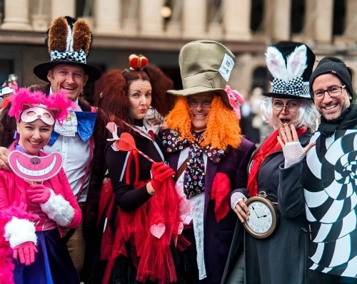 A group of six people in colorful costumes, including hats and wigs, posing playfully in a festive setting.