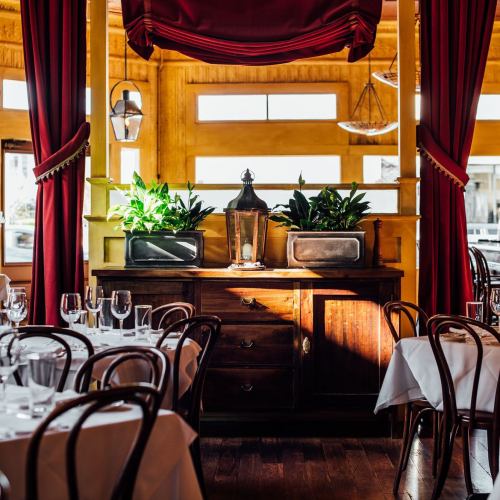 Cozy restaurant interior with wooden furniture, potted plants, and elegantly set tables under warm yellow walls.