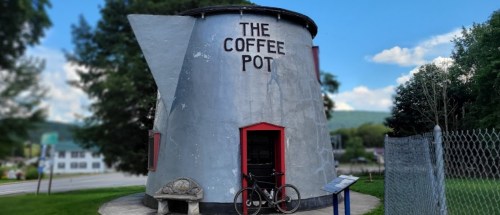 A large, whimsical building shaped like a coffee pot, with a bike parked outside and trees in the background.