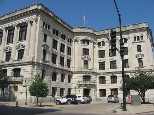 Historic building with a classical architectural style, featuring large windows and a flag on top, set against a clear blue sky.