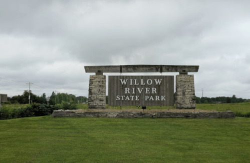 Sign for Willow River State Park, featuring stone pillars and a grassy area under a cloudy sky.