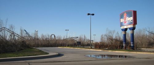Sign for Six Flags amusement park with roller coasters visible in the background on a clear day.