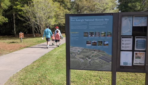 Visitors walking along a path at Fort Raleigh National Historic Site, with an informational sign nearby.
