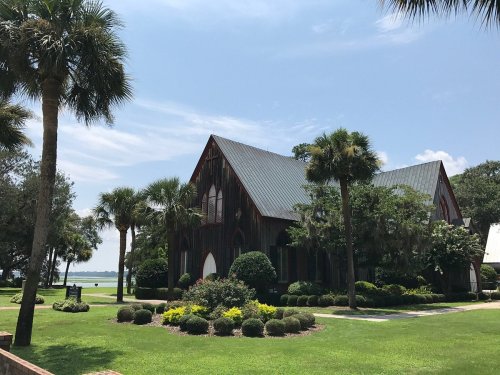 A charming wooden church surrounded by lush greenery and palm trees, with a view of the water in the background.