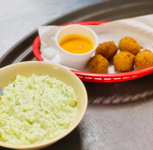 A bowl of creamy green coleslaw next to a red tray with golden fried balls and a small cup of dipping sauce.