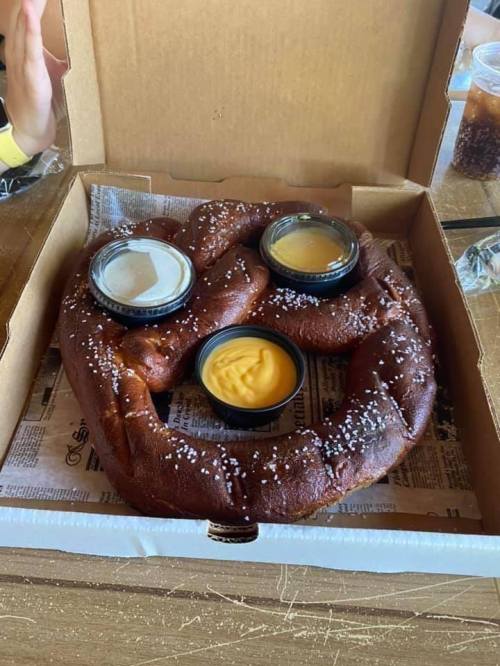 A large pretzel in a box, topped with coarse salt and served with three dipping sauces.