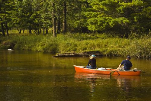 Two people in a red canoe on a calm river, surrounded by lush greenery and trees.