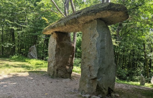 A large stone structure resembling a dolmen, surrounded by trees in a forested area.