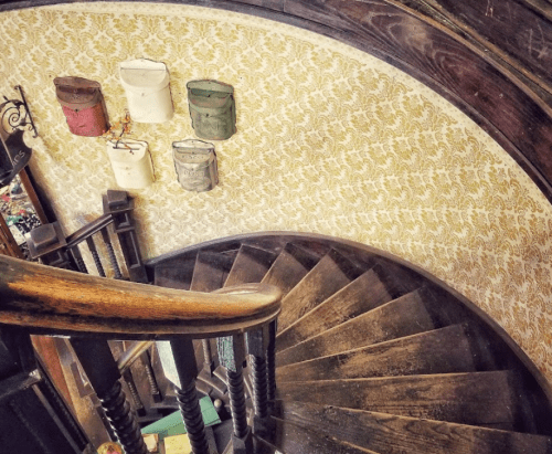 A spiral staircase with wooden steps, leading down, and vintage buckets hanging on the wall.