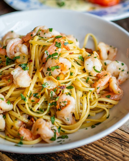 A bowl of linguine pasta topped with shrimp and garnished with parsley.
