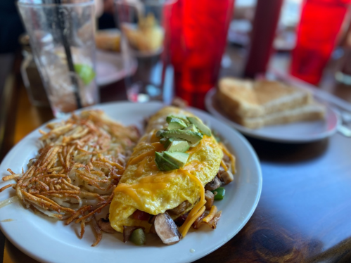 A plate of a cheese omelet topped with avocado, hash browns, and toast, served in a restaurant setting.