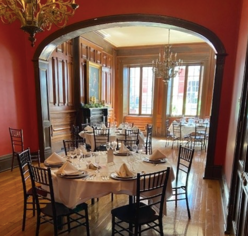 Elegant dining room with wooden accents, round tables set for a meal, and large windows letting in natural light.