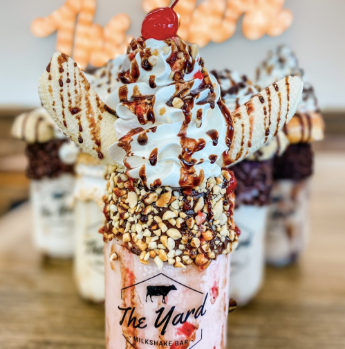 A decadent milkshake topped with whipped cream, a cherry, and cookie wings, surrounded by other milkshakes in the background.