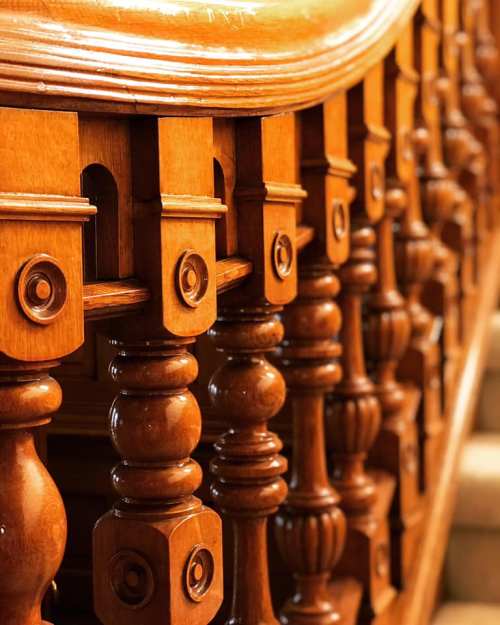 Close-up of a wooden staircase railing with intricate carvings and round balusters. Warm tones and smooth finish.