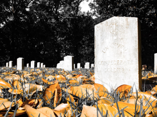 Gravestones in a cemetery, with a focus on a marker for an "Unknown Confederate Soldier" surrounded by autumn leaves.