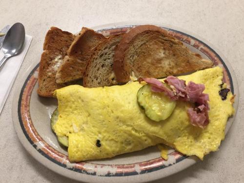 A plate with a yellow omelet filled with pickles and ham, accompanied by slices of toasted bread.