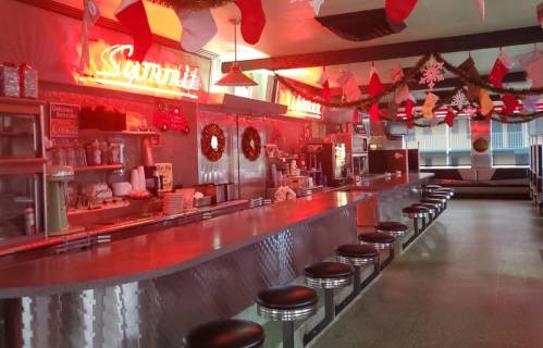 A retro diner with a long counter, festive decorations, and red neon signs, creating a cozy holiday atmosphere.