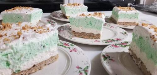 Slices of mint green dessert with whipped cream and crushed nuts, served on floral-patterned plates.