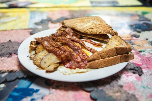 A plate of crispy bacon, fried potatoes, and two slices of toasted bread with a sunny-side-up egg.