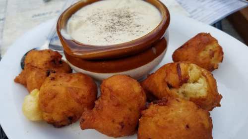 A plate featuring a bowl of creamy soup topped with pepper, surrounded by golden, fried dough balls.