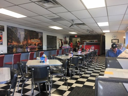 A retro diner interior with checkered floors, tables, and red booths, featuring vintage decor and a casual atmosphere.