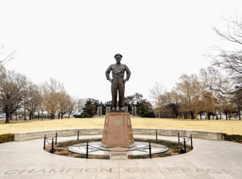 Statue of a man in uniform, titled "Champion of Peace," surrounded by a landscaped area and trees.