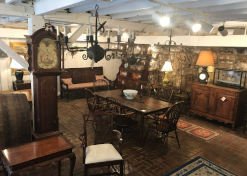 A cozy room featuring antique furniture, including a dining table, chairs, a clock, and various decorative items.