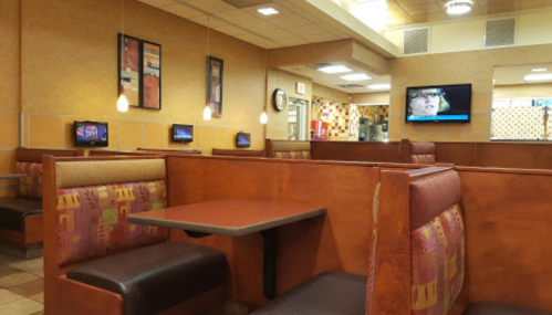 Interior of a fast-food restaurant with empty booths, a TV on the wall, and warm lighting.