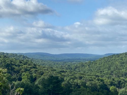 A panoramic view of lush green hills under a partly cloudy sky, showcasing a serene natural landscape.