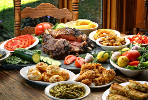 A table spread with a variety of dishes, including roasted meat, vegetables, fried chicken, and sides.