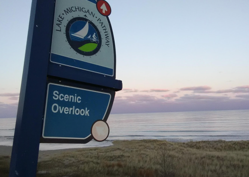 Sign for "Scenic Overlook" near Lake Michigan, with calm waters and a pastel sky in the background.